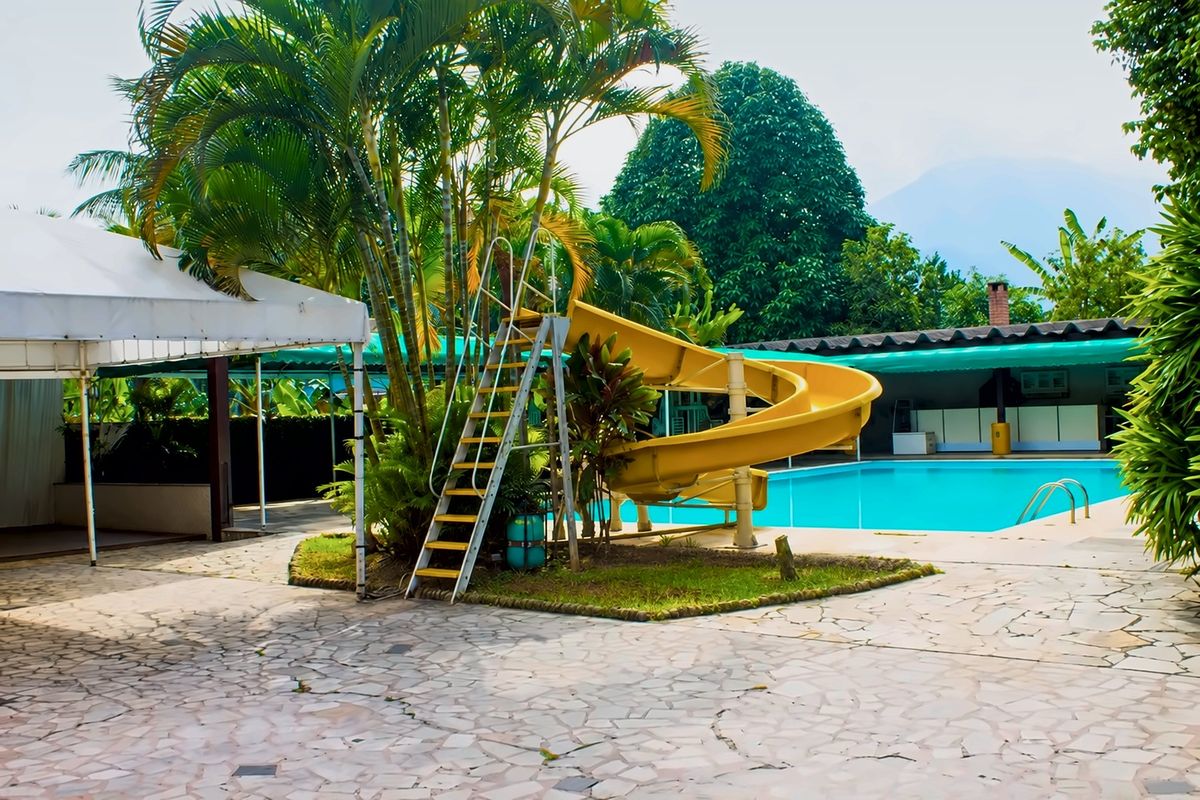 Piscina com toboágua amarelo entre palmeiras, com a montanha ao fundo